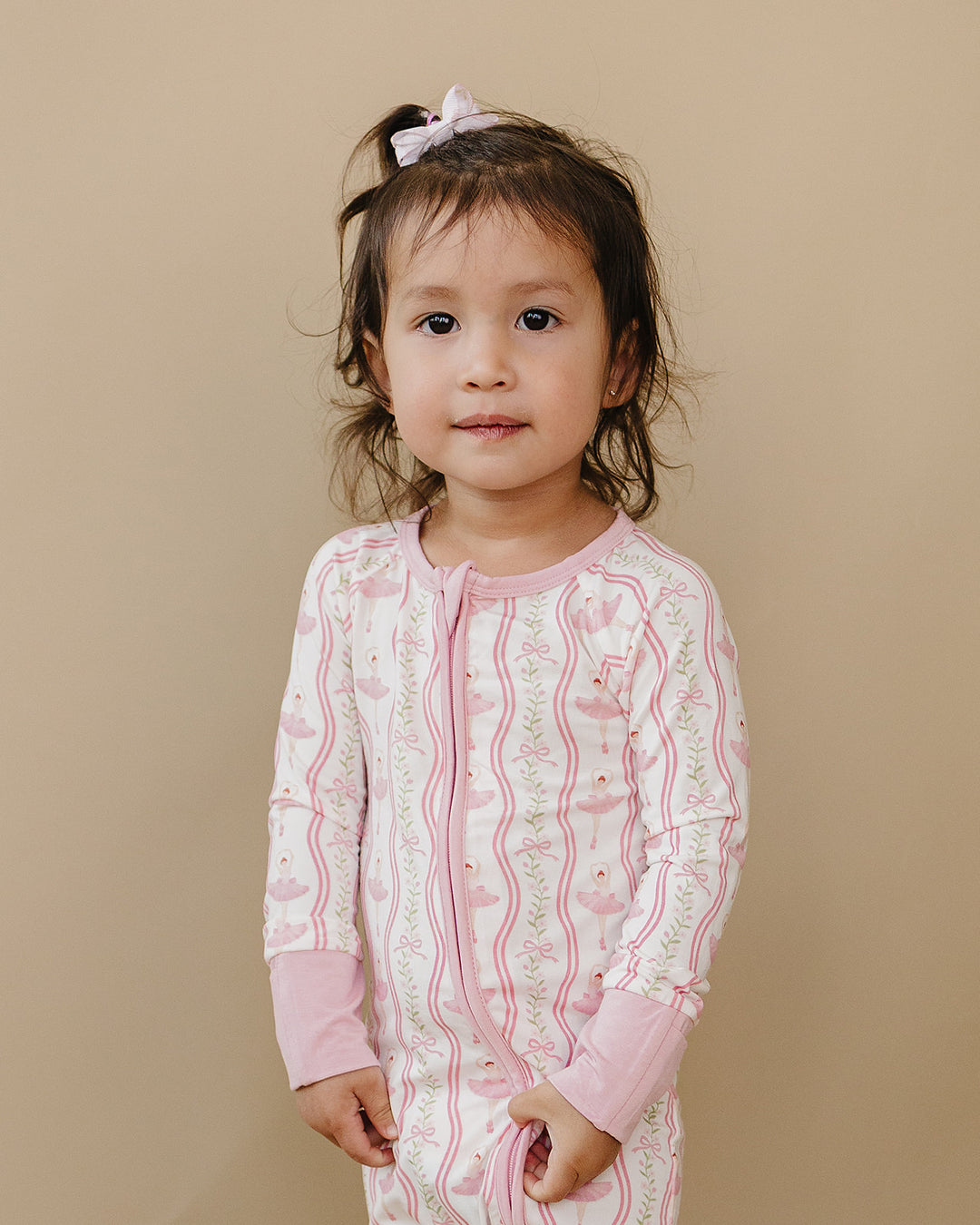 Toddler modeling the Little Ballerina bamboo zip romper against a neutral beige background.