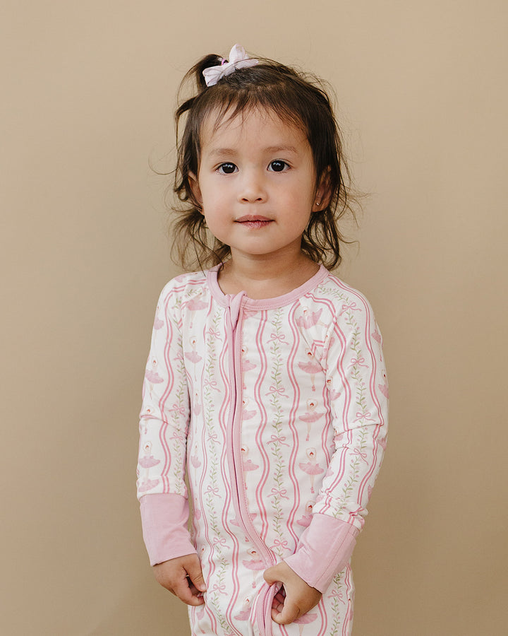 Toddler modeling the Little Ballerina bamboo zip romper against a neutral beige background.