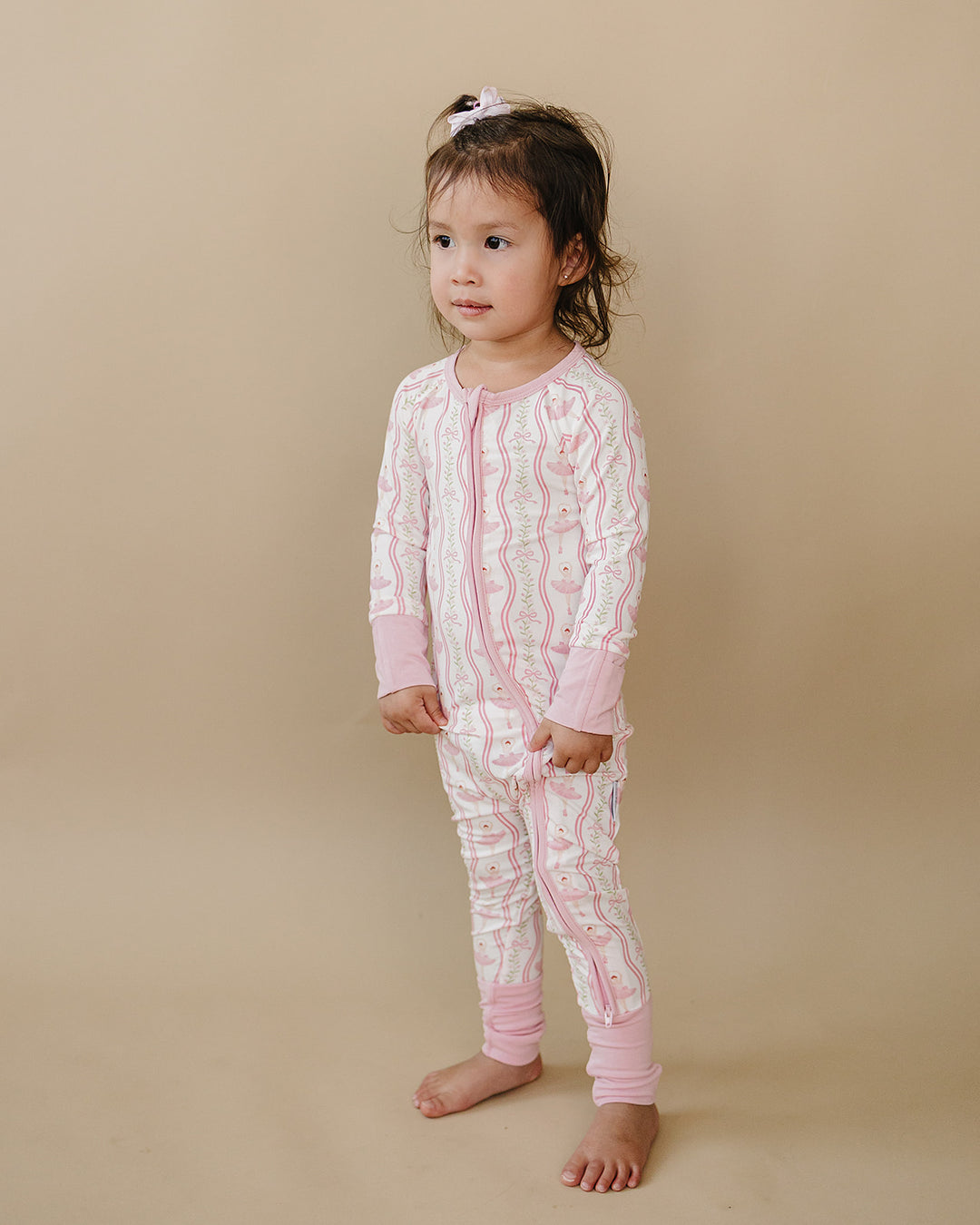 Child standing in the Little Ballerina bamboo zip romper against a beige background.