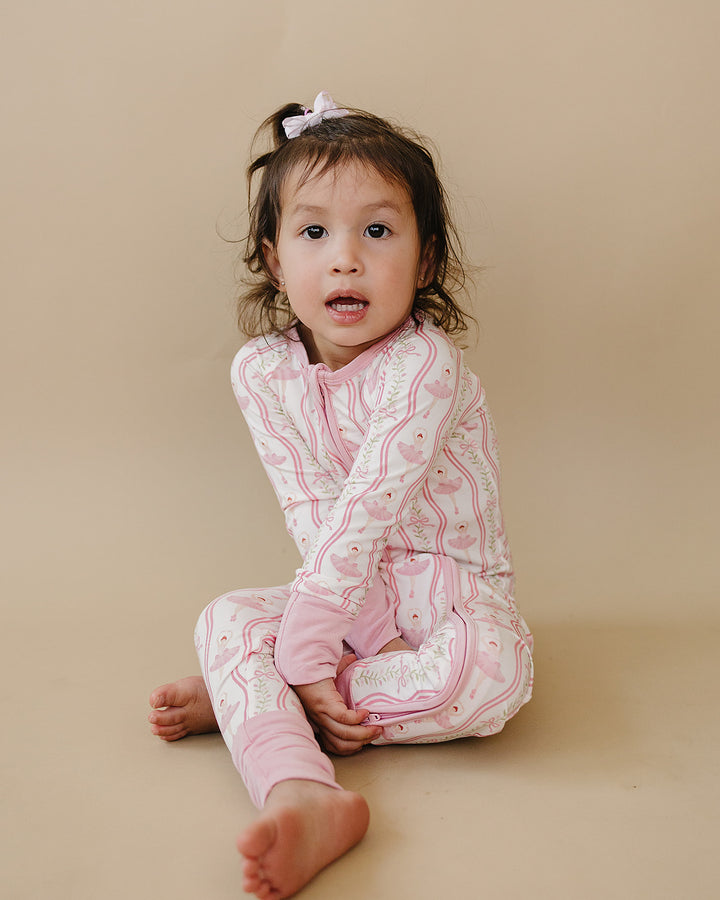 Toddler sitting in the Little Ballerina bamboo zip romper against a neutral background.
