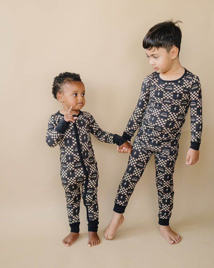 Two children holding hands in coordinating Long Live Boyhood bamboo romper and two-piece set.