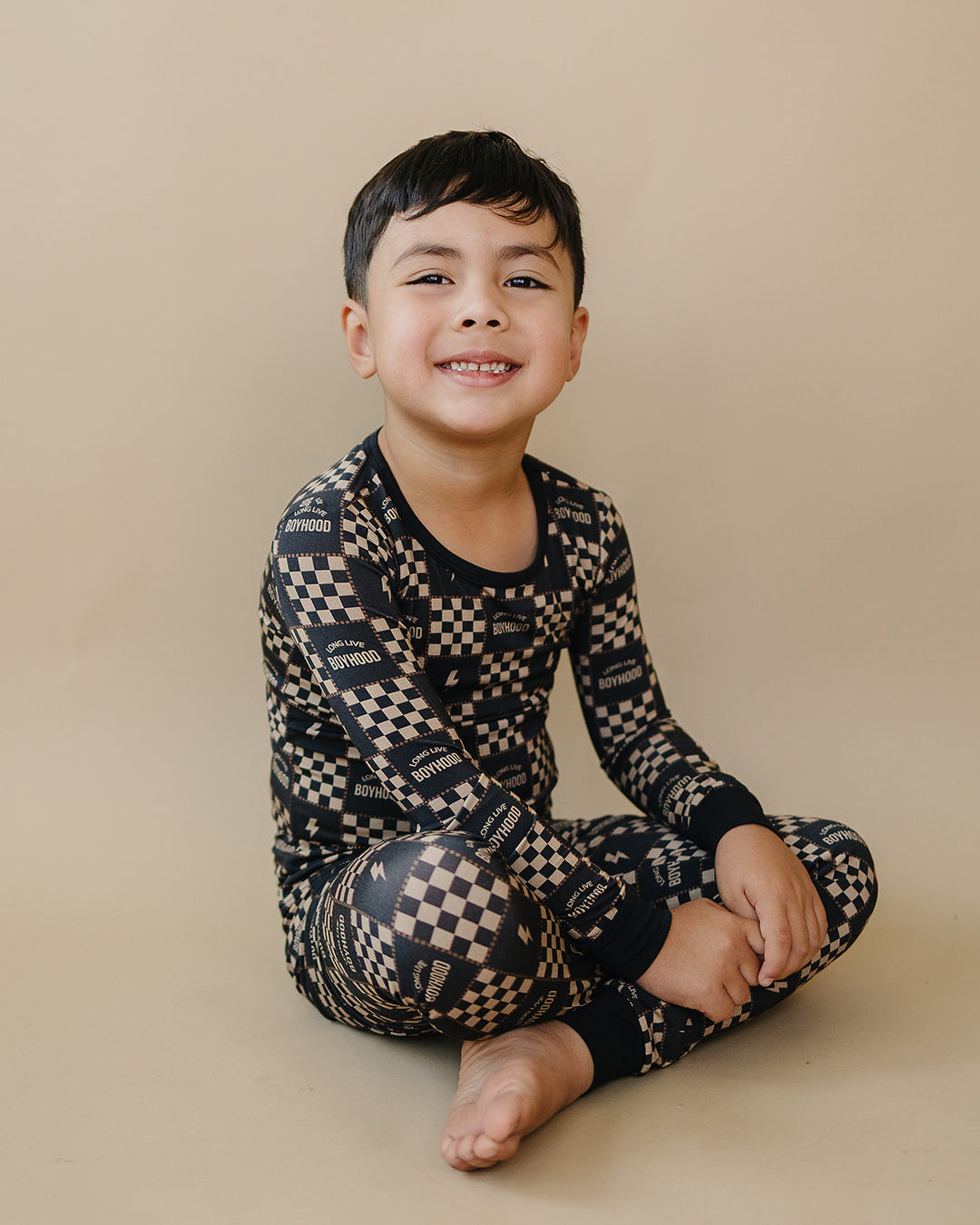 Smiling child seated in the Long Live Boyhood long-sleeve bamboo top and matching pants.