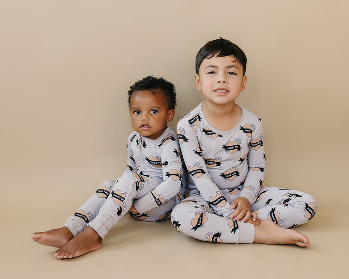 Two children seated together in coordinating Mama’s Boy bamboo zip romper and two-piece set.