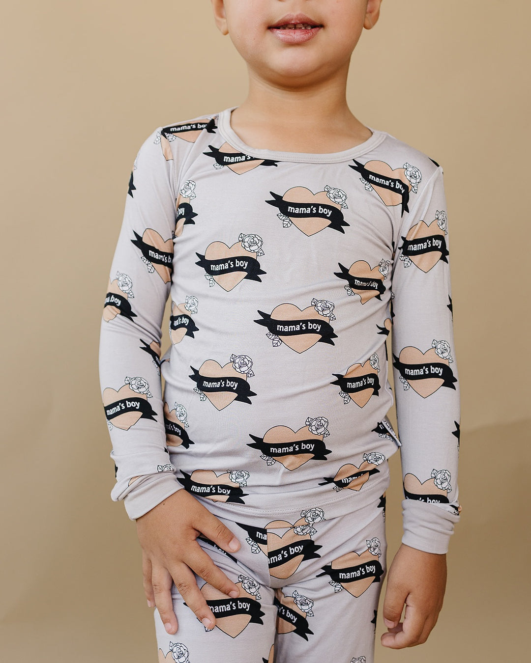Close-up of a child wearing the Mama’s Boy bamboo two-piece set with beige hearts and black “mama’s boy” banners.