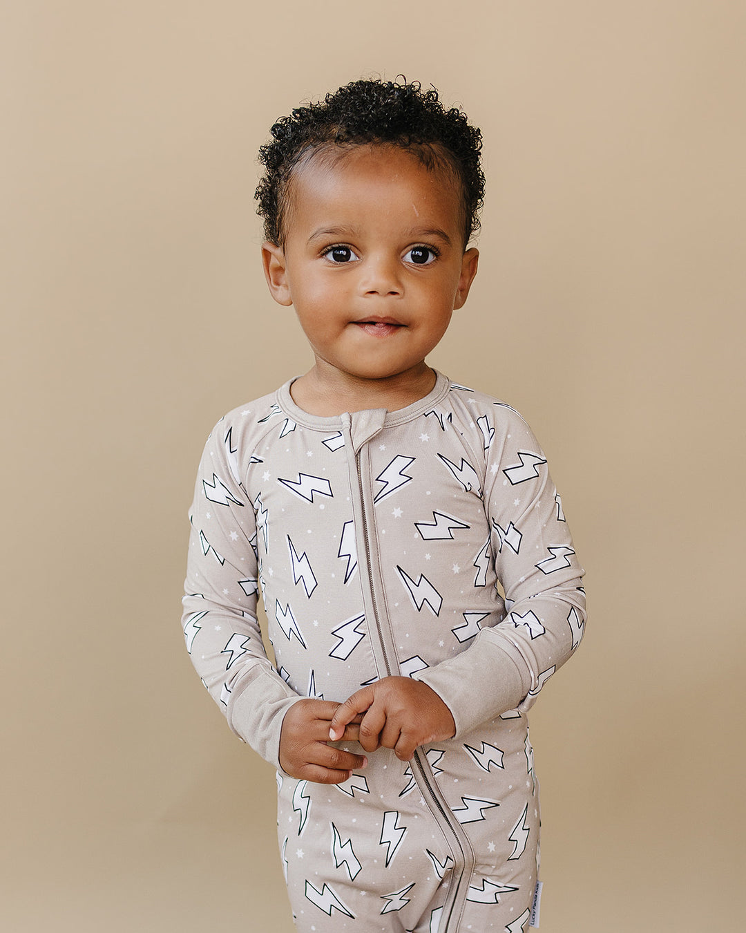 Toddler boy modeling the Lucky Panda Kids Latte Bolts bamboo zip romper in a taupe lightning bolt print.