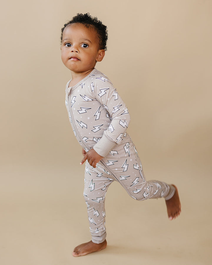 Side view of a toddler boy wearing the Latte Bolts bamboo zip romper with one leg lifted playfully.