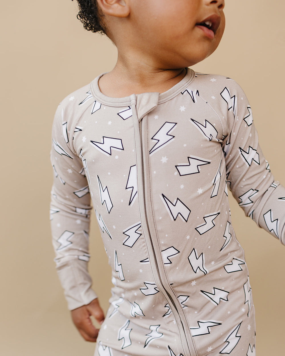 Close-up of a child wearing the Latte Bolts bamboo zip romper, showing the two-way zipper and white lightning bolt print.