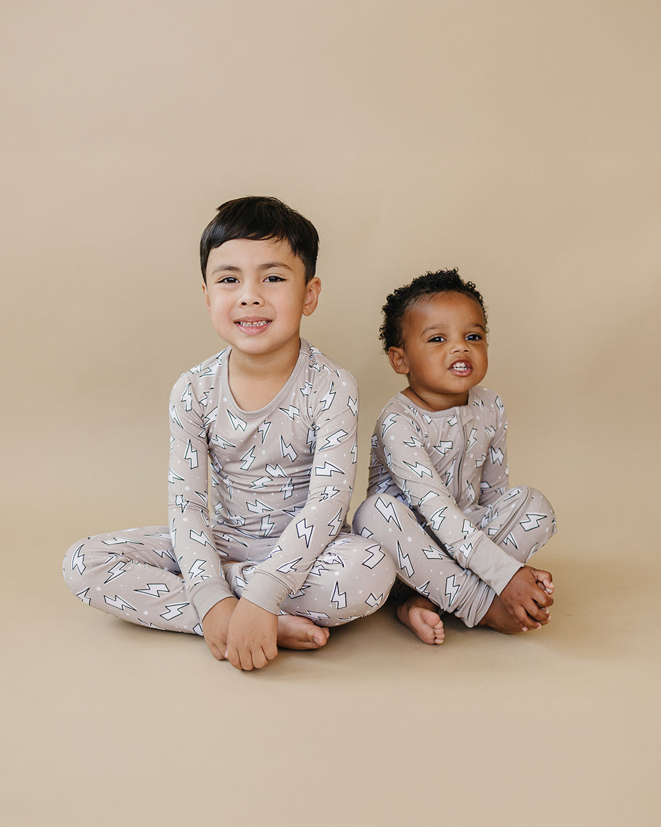 Side view of a toddler boy wearing the Latte Bolts bamboo zip romper with one leg lifted playfully.