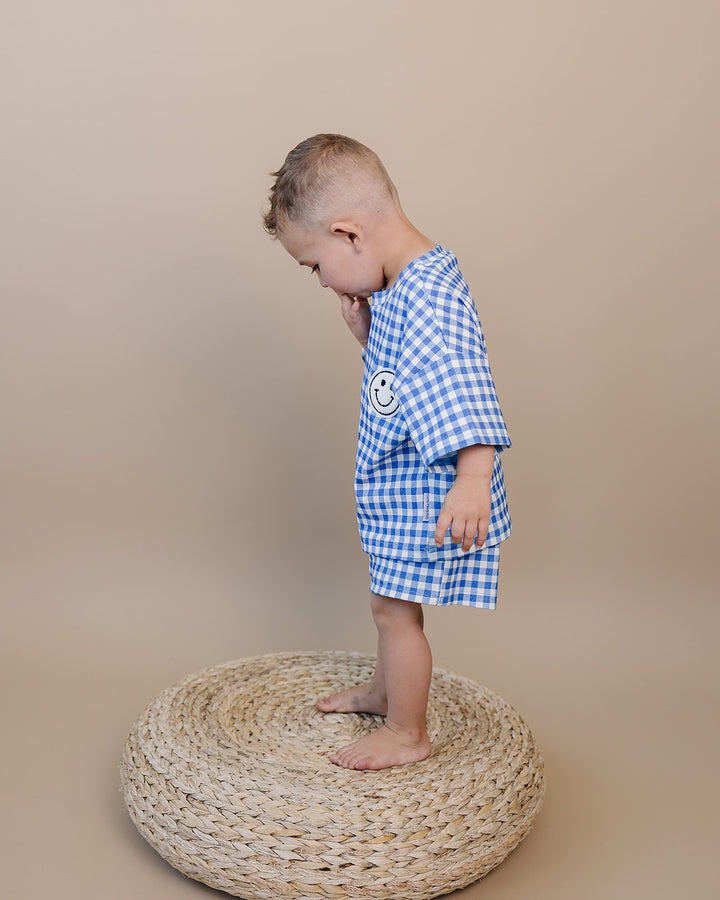 Baby wearing Lucky Panda Kids Blue Gingham Shorts Set — gender neutral cotton two-piece with smiley face patch
Lucky Panda Kids Shorts Set Blue Gingham flat lay — relaxed top with smiley patch and matching elastic waistband shorts
Toddler in Lucky Panda Kids Blue Gingham Shorts Set — sizes 0–3M to 8–9Y, gender neutral summer outfit
Close-up of Lucky Panda Kids Blue Gingham Shorts Set smiley face patch — soft 95% cotton kids two-piece
Lucky Panda Kids Blue Gingham Shorts Set on babies — gender neutral cotton