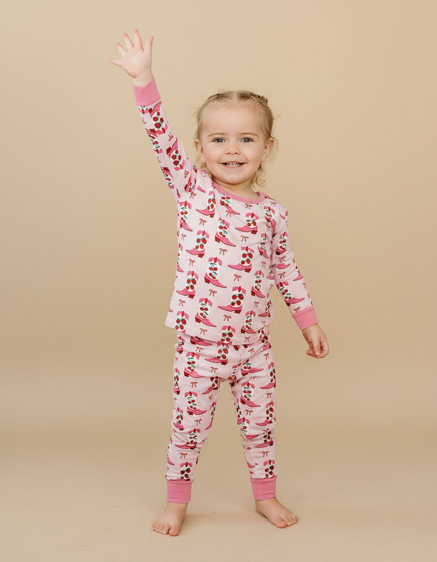 Child wearing a pink and red patterned cherry pajama set on a beige background