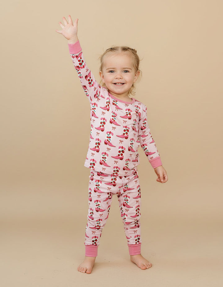 Child wearing a pink and red patterned cherry pajama set on a beige background