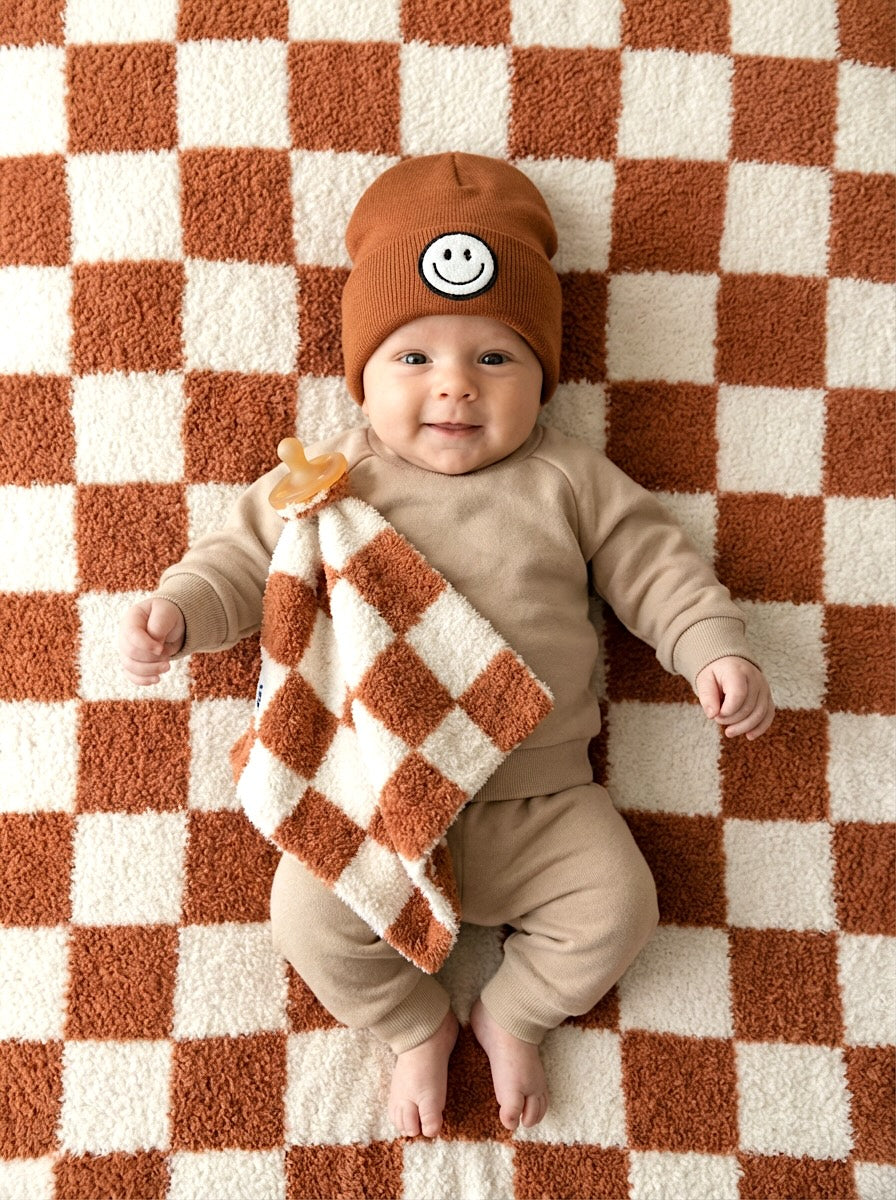 Baby wearing a brown outfit with a checkered blanket rug