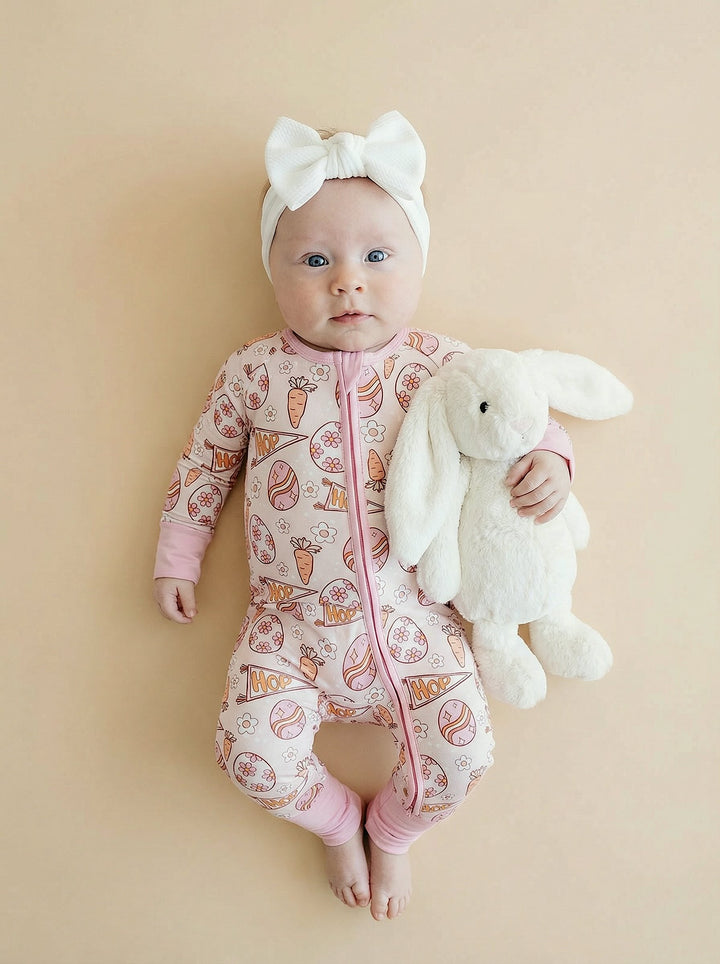 Baby in a pink easter ooutfit with a white bow and plush toy on a beige background