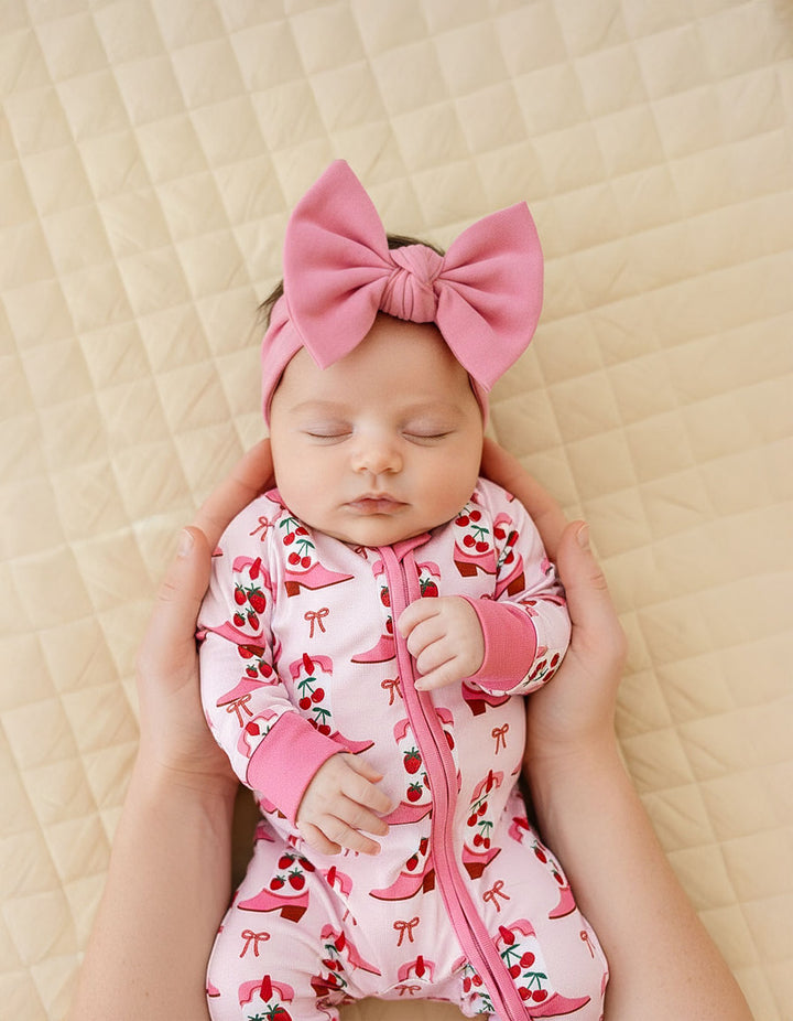 Newborn baby in a pink outfit with a large bow on a beige quilted background
