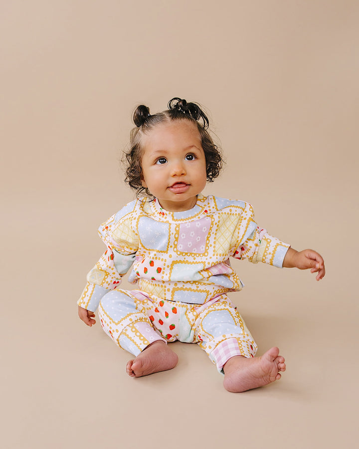 Baby sitting with one arm extended while wearing the Sweet Patchwork jogger set with pastel printed squares.