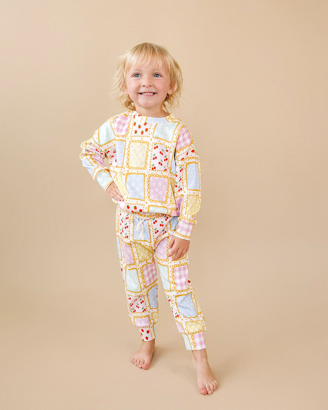 Smiling child wearing the Sweet Patchwork jogger set with pastel squares, strawberry prints and yellow borders.