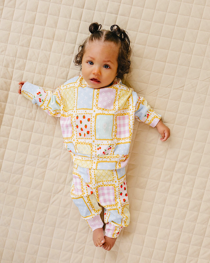 Baby lying with arms out on a cream quilt in the Sweet Patchwork jogger set with feet uncovered.