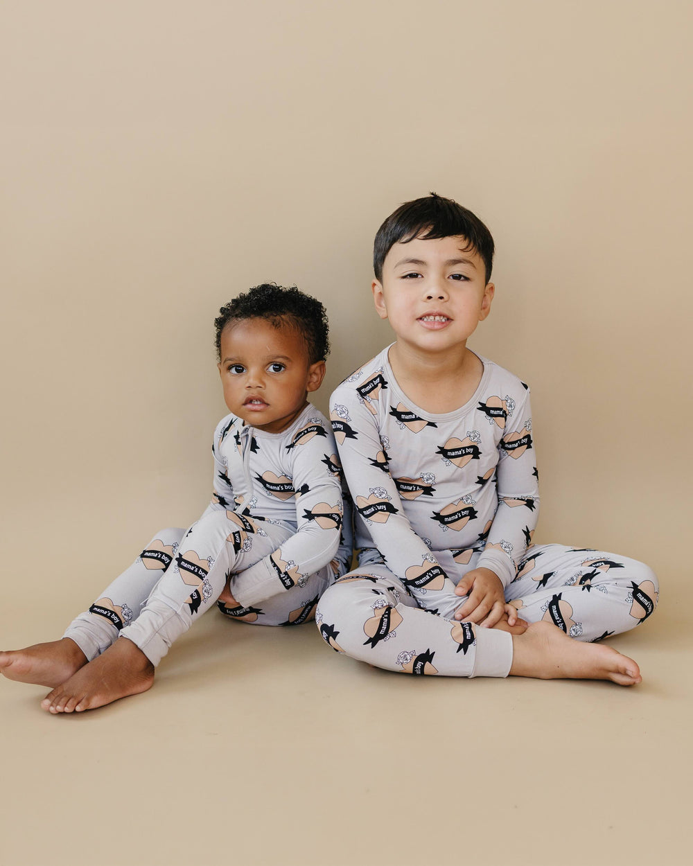 Two children sitting together in coordinating Mama’s Boy bamboo romper and two-piece set.