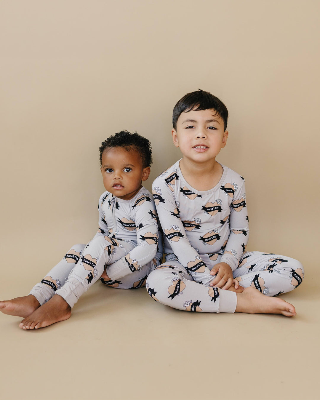 Two children sitting together in coordinating Mama’s Boy bamboo romper and two-piece set.