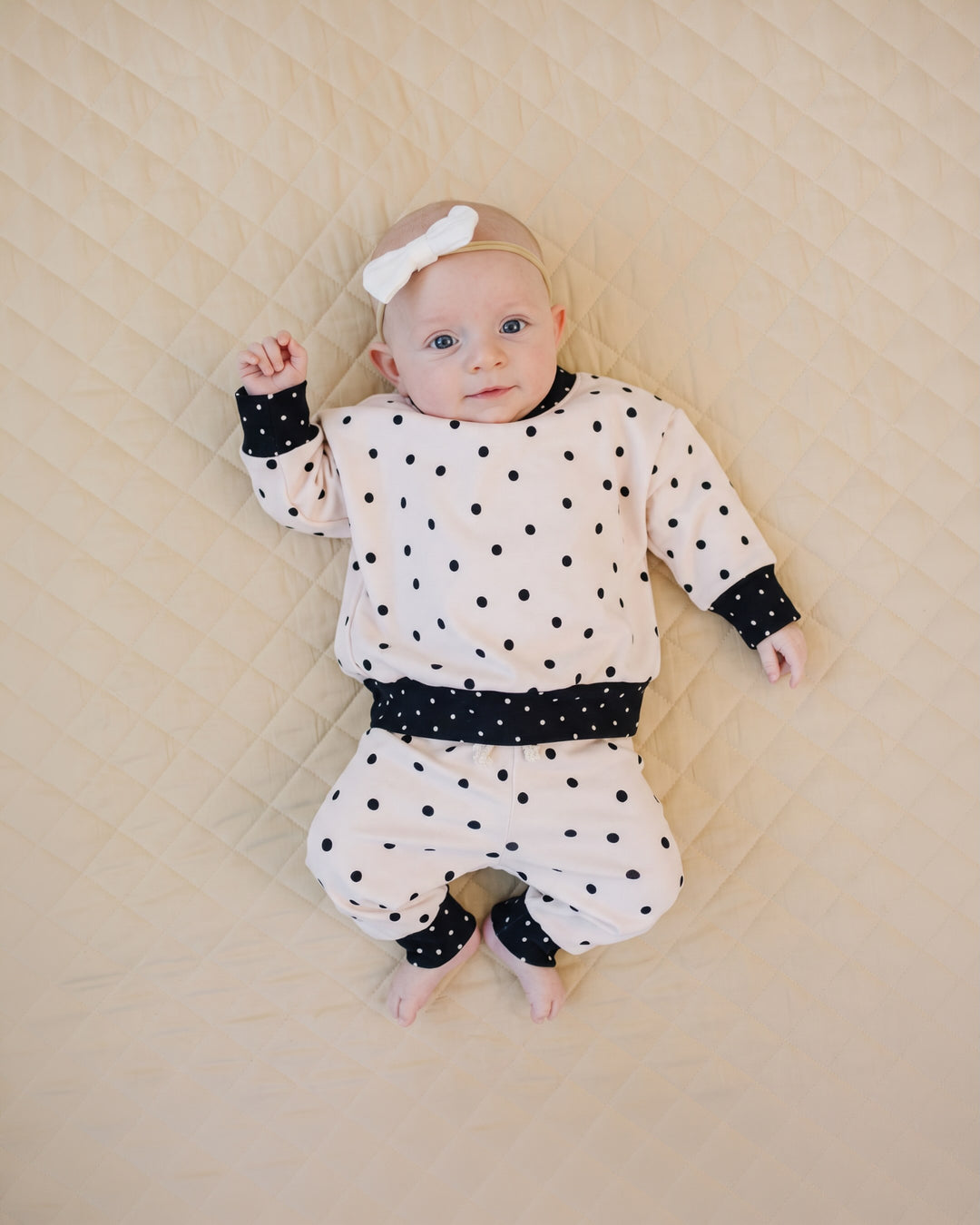 Baby wearing the Classic Polka Jogger Set while lying on a quilted blanket