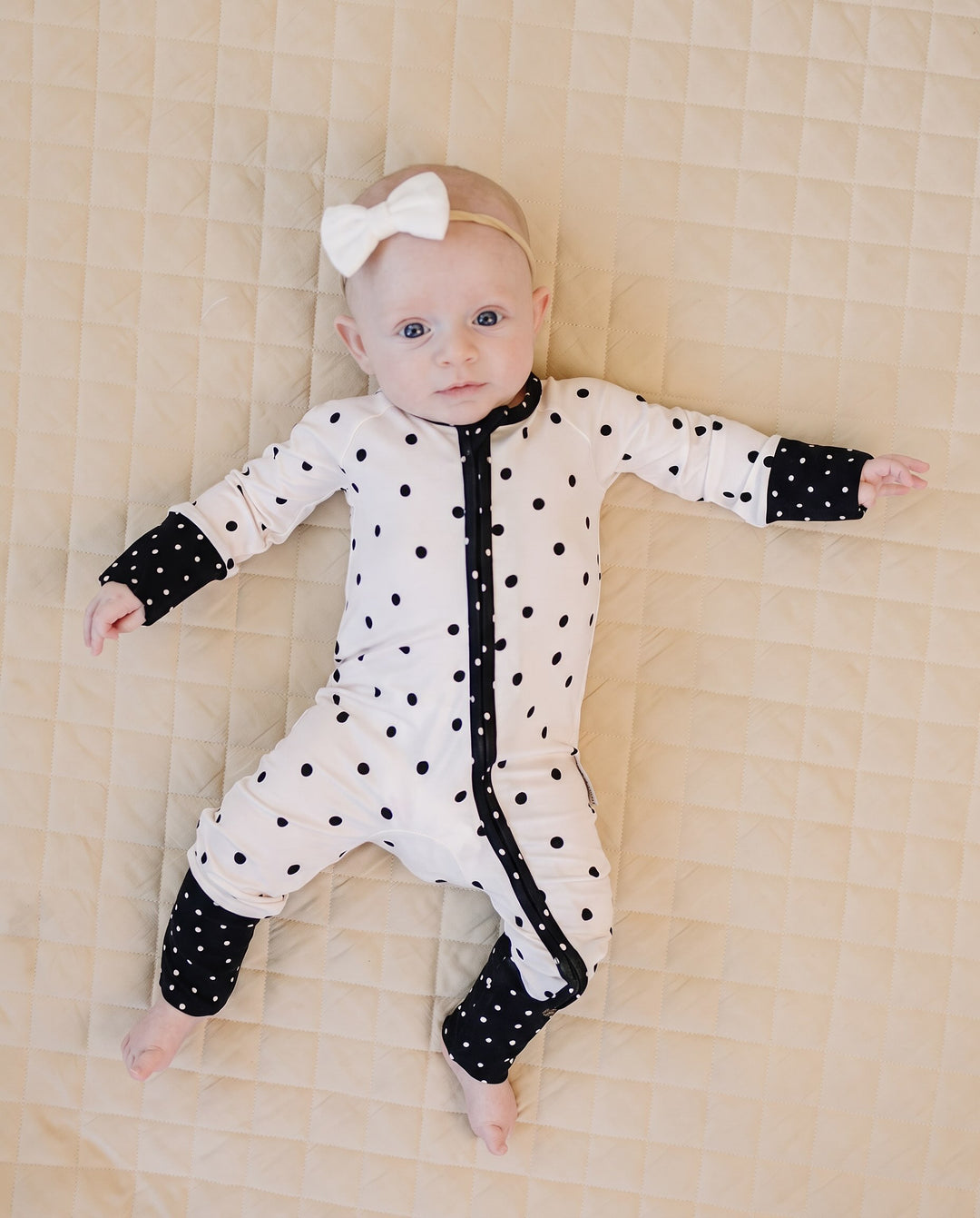 Baby wearing the Classic Polka Bamboo Zip Romper in a black polka dot print on white
