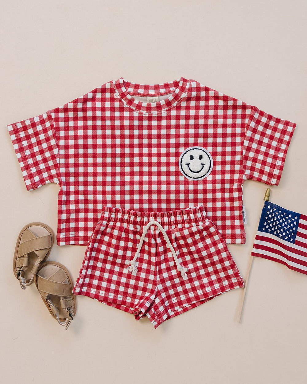 Baby wearing Lucky Panda Kids Red Gingham Shorts Set — gender neutral cotton two-piece with smiley face patch
Lucky Panda Kids Shorts Set Red Gingham flat lay — relaxed top with smiley patch and matching elastic waistband shorts
Toddler in Lucky Panda Kids Red Gingham Shorts Set — sizes 0–3M to 8–9Y, gender neutral summer outfit
Close-up of Lucky Panda Kids Red Gingham Shorts Set smiley face patch — soft 95% cotton kids two-piece
Lucky Panda Kids Red Gingham Shorts Set on baby — gender neutral cotton summer