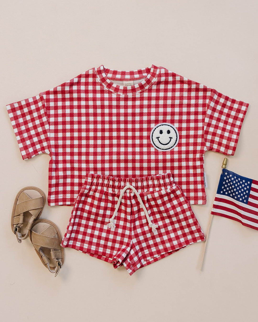 Baby wearing Lucky Panda Kids Red Gingham Shorts Set — gender neutral cotton two-piece with smiley face patch
Lucky Panda Kids Shorts Set Red Gingham flat lay — relaxed top with smiley patch and matching elastic waistband shorts
Toddler in Lucky Panda Kids Red Gingham Shorts Set — sizes 0–3M to 8–9Y, gender neutral summer outfit
Close-up of Lucky Panda Kids Red Gingham Shorts Set smiley face patch — soft 95% cotton kids two-piece
Lucky Panda Kids Red Gingham Shorts Set on baby — gender neutral cotton summer