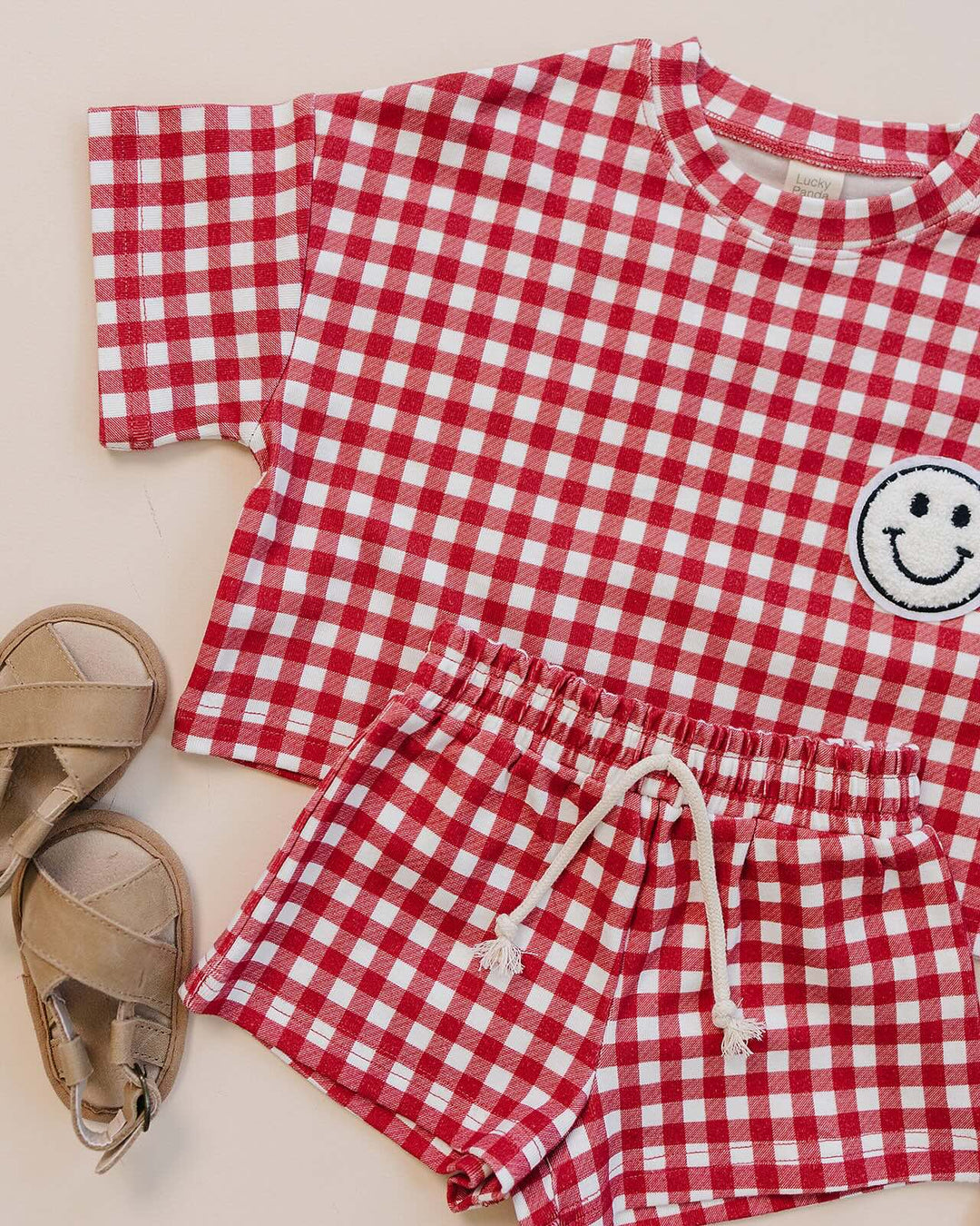 Baby wearing Lucky Panda Kids Red Gingham Shorts Set — gender neutral cotton two-piece with smiley face patch
Lucky Panda Kids Shorts Set Red Gingham flat lay — relaxed top with smiley patch and matching elastic waistband shorts
Toddler in Lucky Panda Kids Red Gingham Shorts Set — sizes 0–3M to 8–9Y, gender neutral summer outfit
Close-up of Lucky Panda Kids Red Gingham Shorts Set smiley face patch — soft 95% cotton kids two-piece
Lucky Panda Kids Red Gingham Shorts Set on baby — gender neutral cotton summer