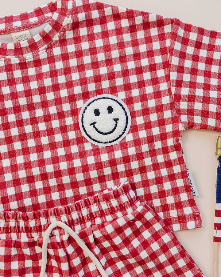 Baby wearing Lucky Panda Kids Red Gingham Shorts Set — gender neutral cotton two-piece with smiley face patch
Lucky Panda Kids Shorts Set Red Gingham flat lay — relaxed top with smiley patch and matching elastic waistband shorts
Toddler in Lucky Panda Kids Red Gingham Shorts Set — sizes 0–3M to 8–9Y, gender neutral summer outfit
Close-up of Lucky Panda Kids Red Gingham Shorts Set smiley face patch — soft 95% cotton kids two-piece
Lucky Panda Kids Red Gingham Shorts Set on baby — gender neutral cotton summer