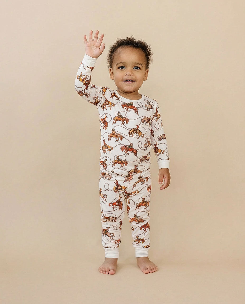 Child wearing a long-sleeve pajama set with rodeo pattern on a beige background