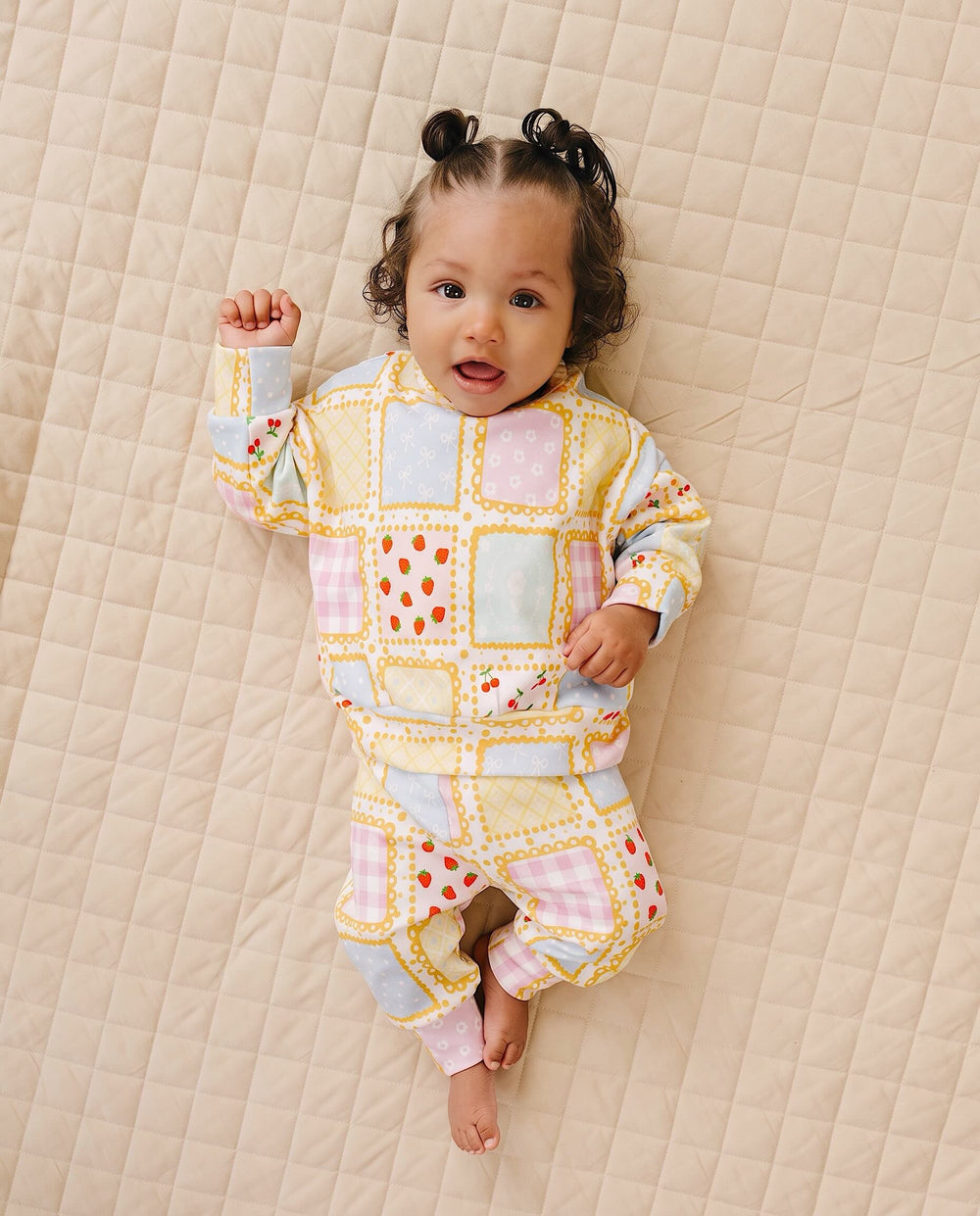 Baby lying on a cream quilt in the Sweet Patchwork top and matching joggers with one knee bent.