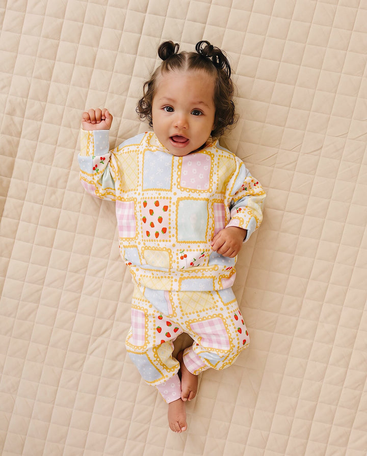 Baby lying on a cream quilt in the Sweet Patchwork top and matching joggers with one knee bent.