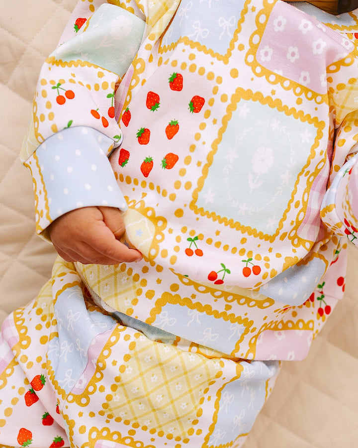 Detail of a baby wearing the Sweet Patchwork top and pants, showing strawberry prints and pale blue cuffs.