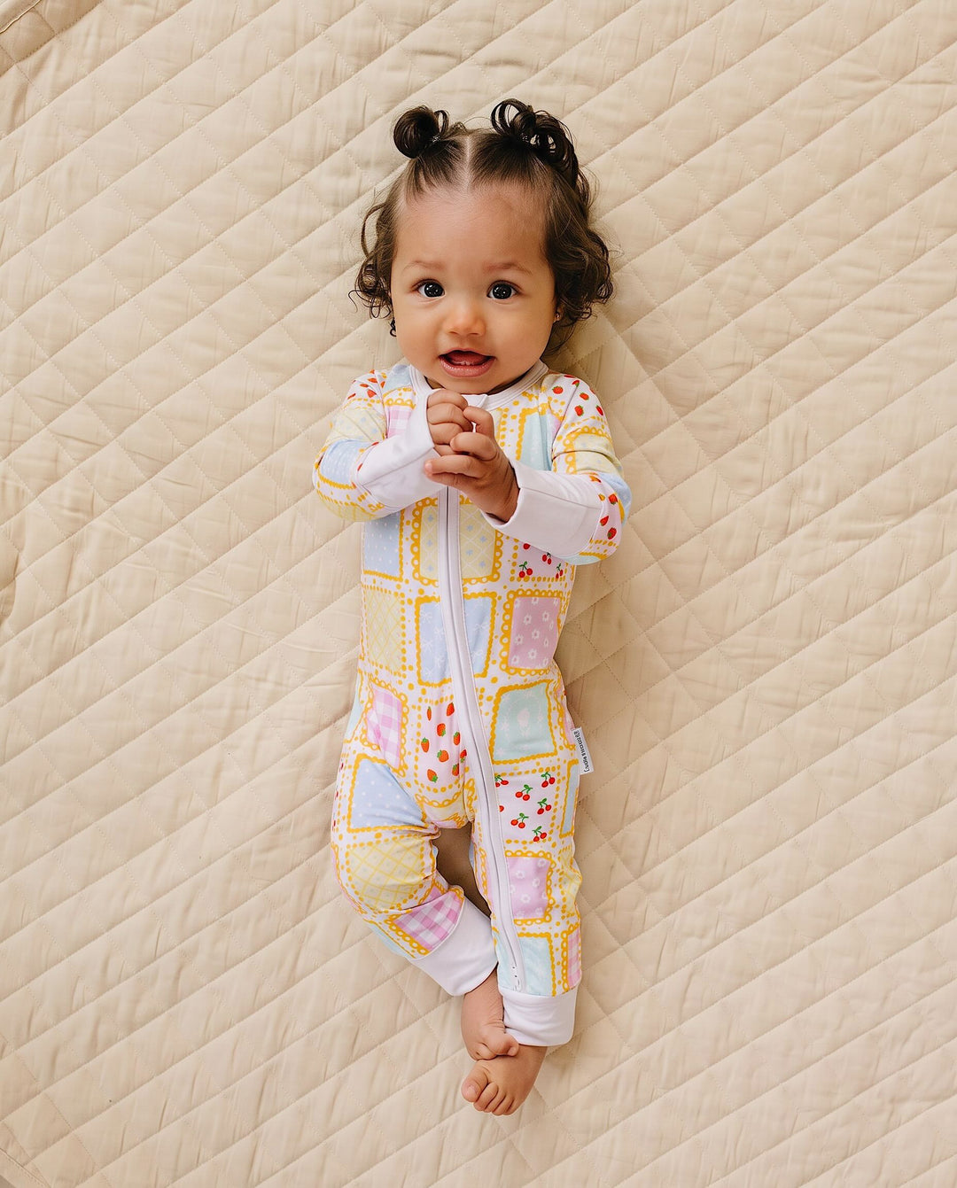 Full length view of a baby holding their hands together in the Sweet Patchwork romper with one knee bent.