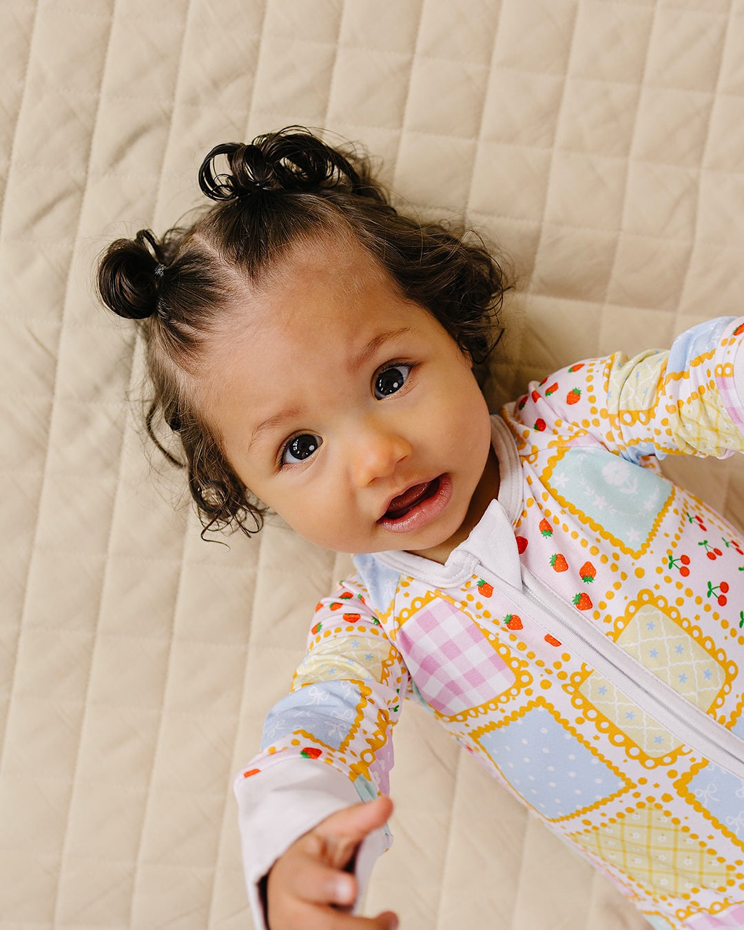 Smiling baby looking up from a cream quilt while wearing the Sweet Patchwork zip romper.