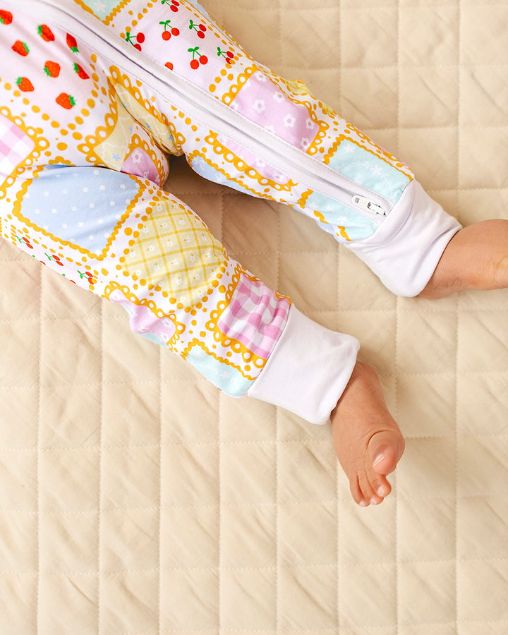 Close up of the Sweet Patchwork romper legs showing pastel squares, white ankle cuffs and uncovered feet on a quilt.