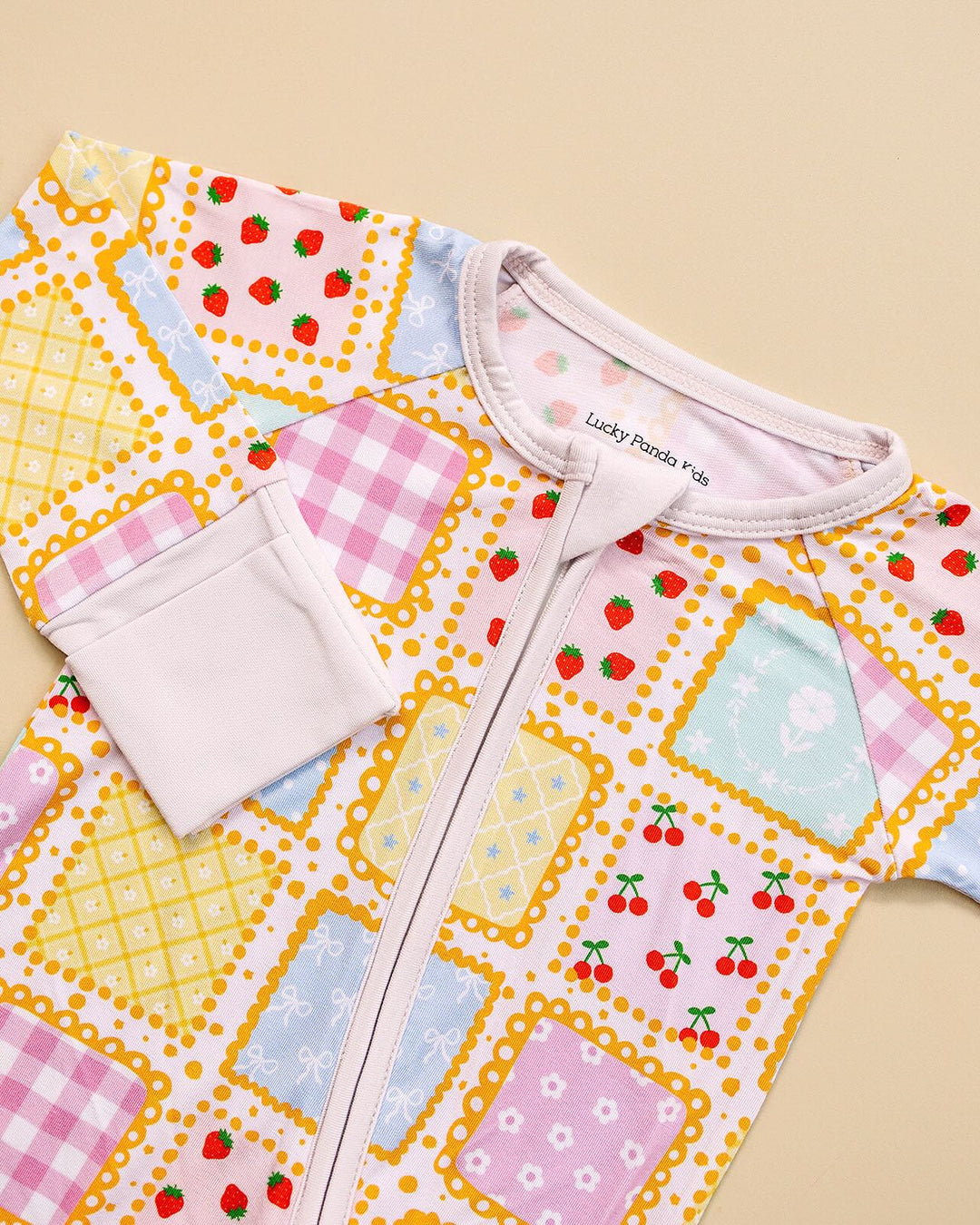 Detail of the Sweet Patchwork romper laid flat, showing the white neckline, zipper and cuff beside strawberry prints.