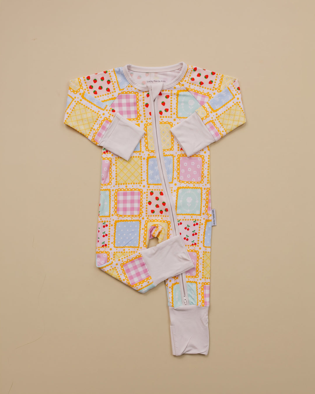 Sweet Patchwork zip romper laid flat with one leg folded, showing long sleeves, pastel squares and white trim.