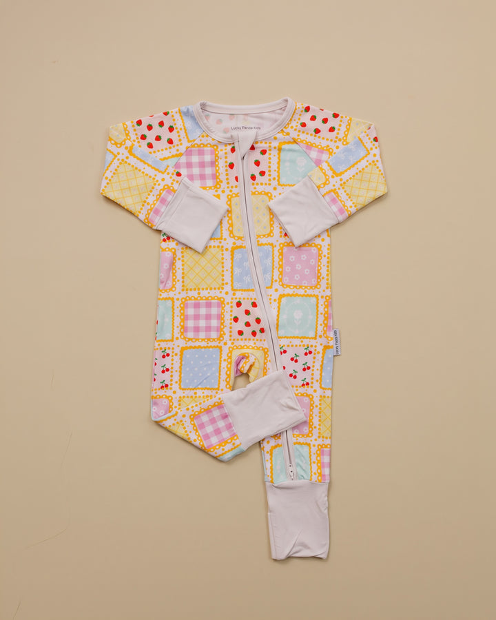 Sweet Patchwork zip romper laid flat with one leg folded, showing long sleeves, pastel squares and white trim.